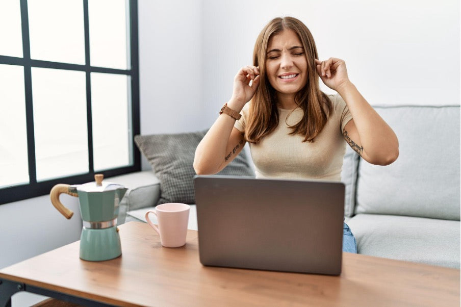 Vrouw die geluiddempende slaap oordoppen indoet terwijl ze werkt aan een laptop, om zich te concentreren in een rumoerige omgeving.